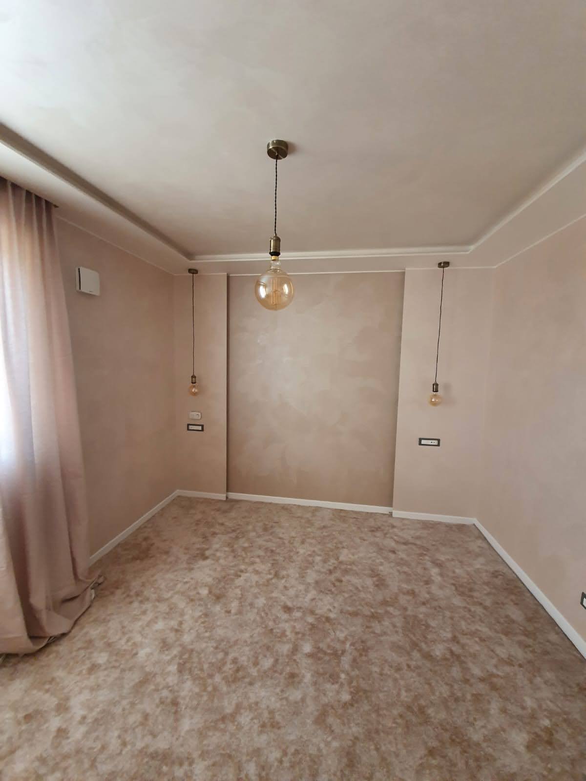 Camera dai toni beige con parete decorativa e lampade sospese